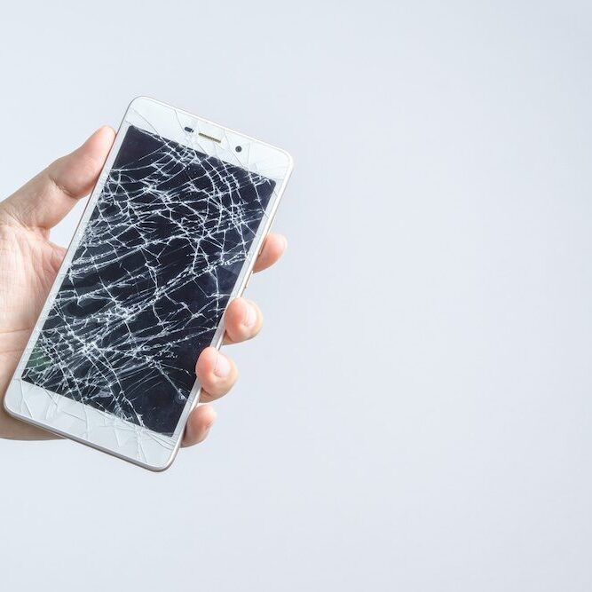 Hand holding mobile phone with broken screen on white background