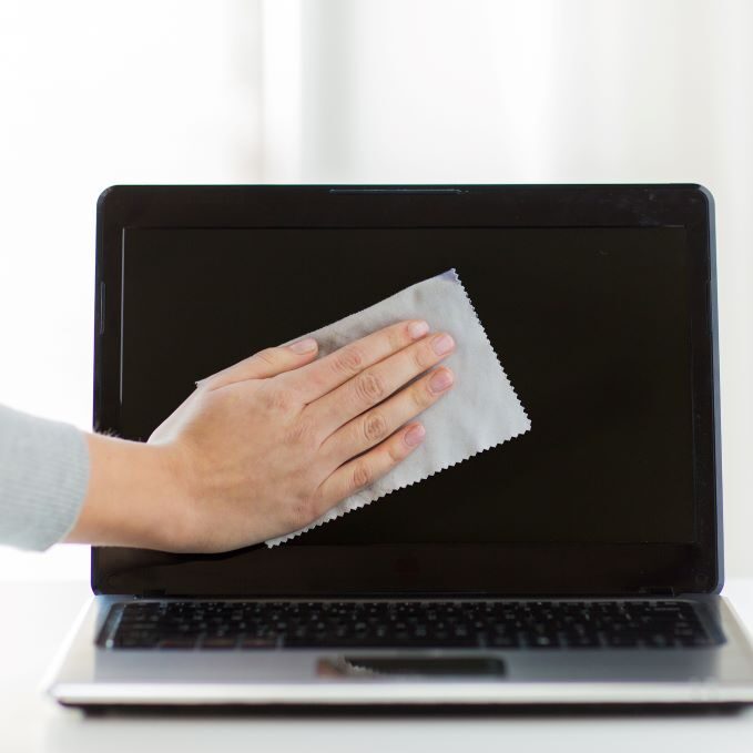 A woman cleaning the screen on her laptop to ensure proper maintenance is followed.